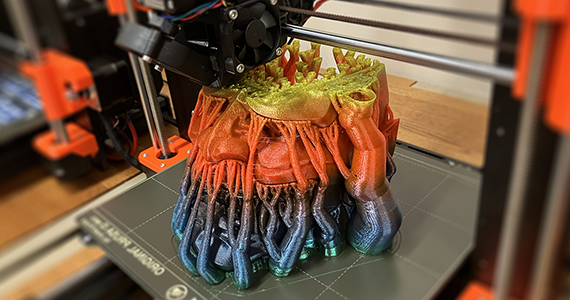 A 3D object is being printed that resembles a head in vibrant colors of red and purple.